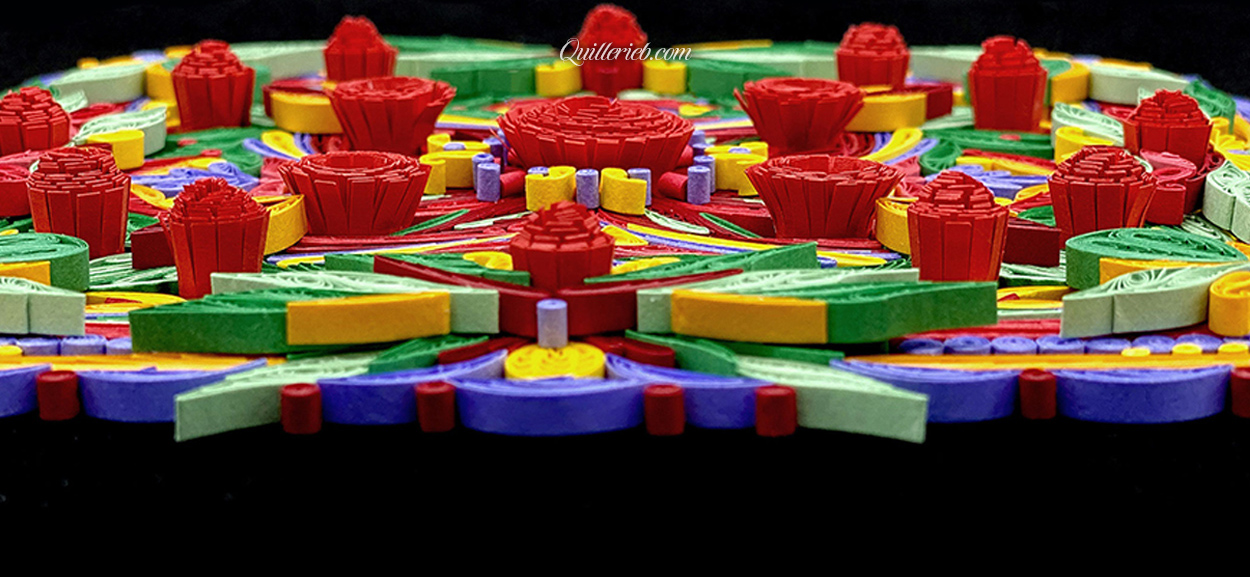 Square-shaped quilling in reds, yellows, greens and purples close-up slanted backwards view.