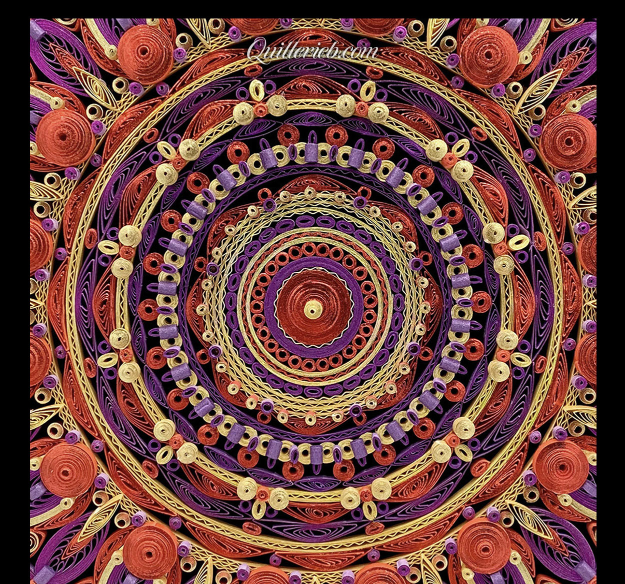 Circular quilled design in red, purple and yellow tones close-up view.