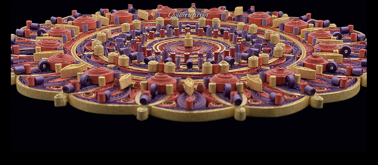 Circular quilled design in red, purple and yellow tones close-up perspective slanted backwards view.