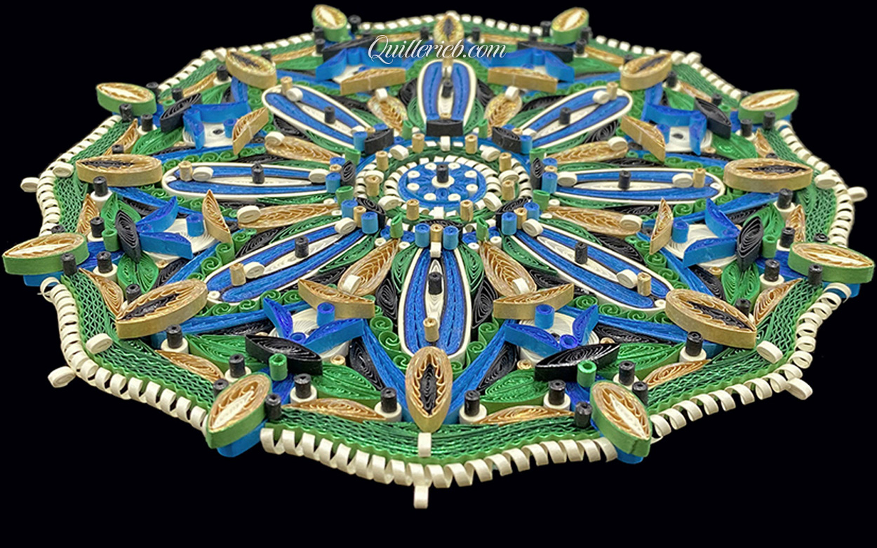 Circular quilled design in green, blue and white tones perspective slanted backwards full view.