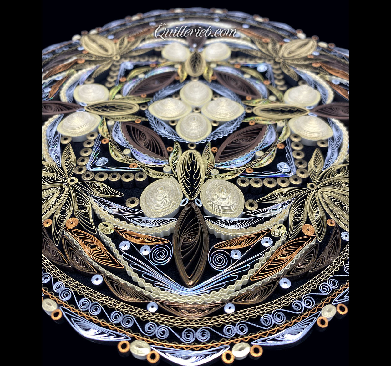 Circular quilled design in muted metallic color tones perspective slanted backwards view.