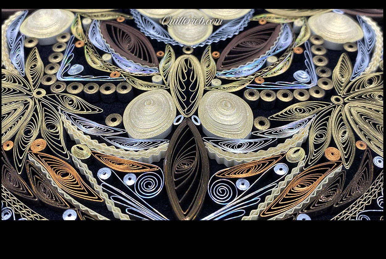 Circular quilled design in muted metallic color tones close-up detail view.