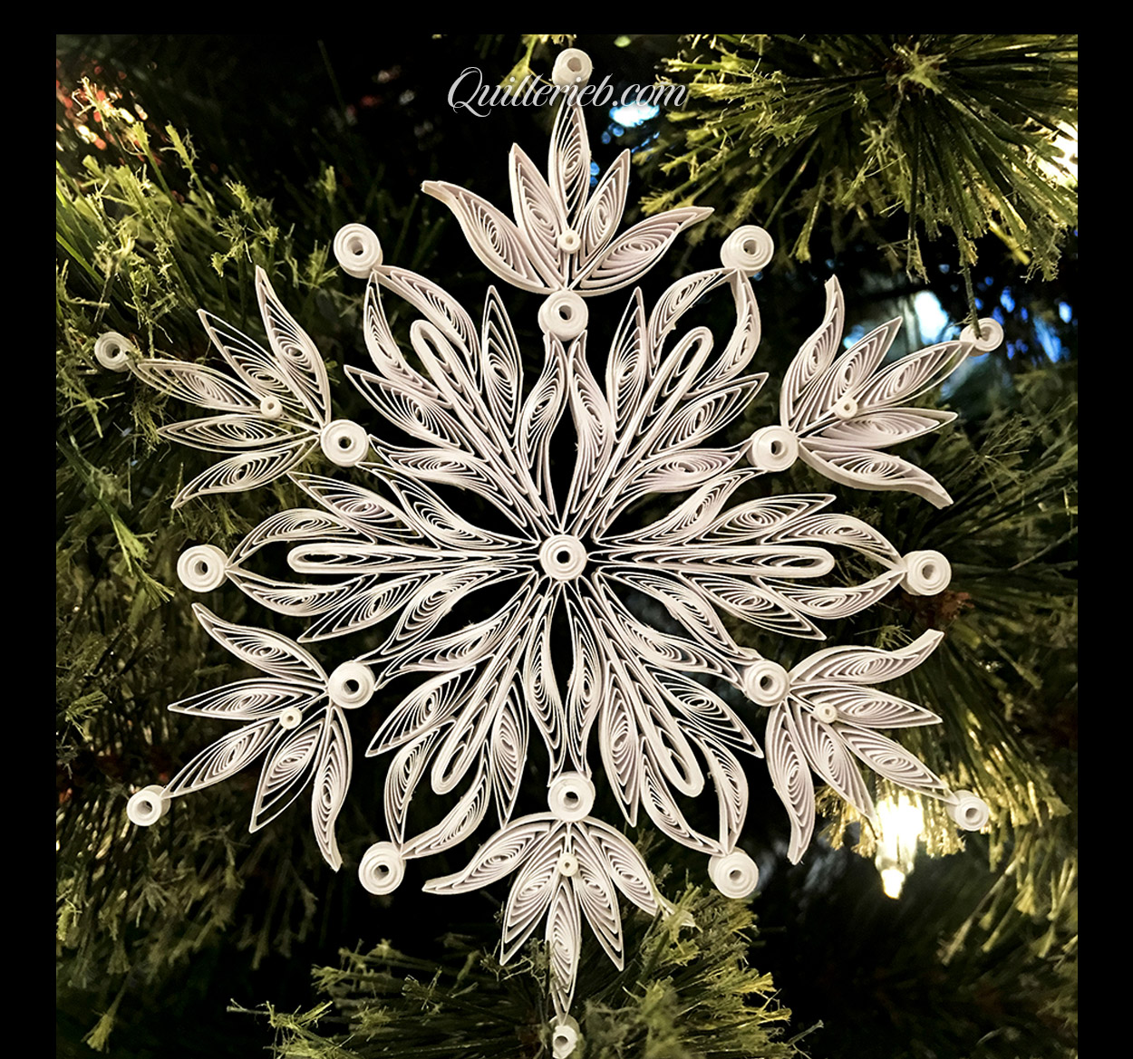  Quilling in white, snowflake design full view against pine wreath backdrop.