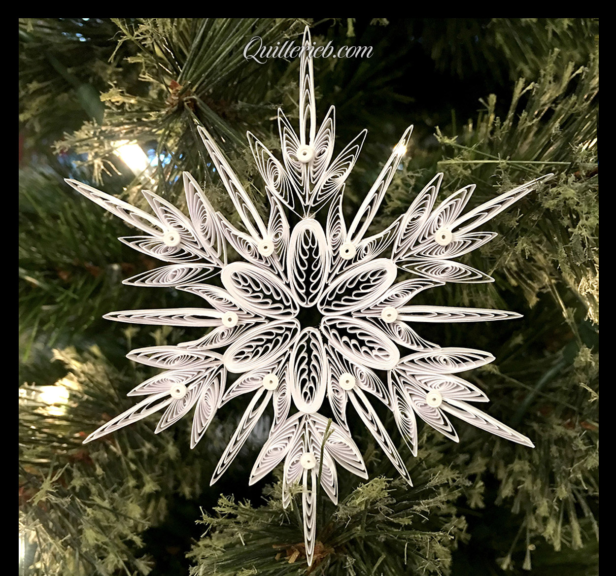  Another quilling in white, snowflake design full view against pine wreath backdrop.