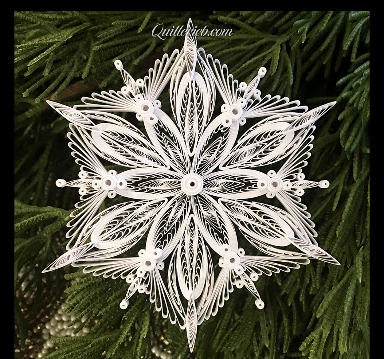  Quilling in white, 4th snowflake design full view against pine wreath backdrop.