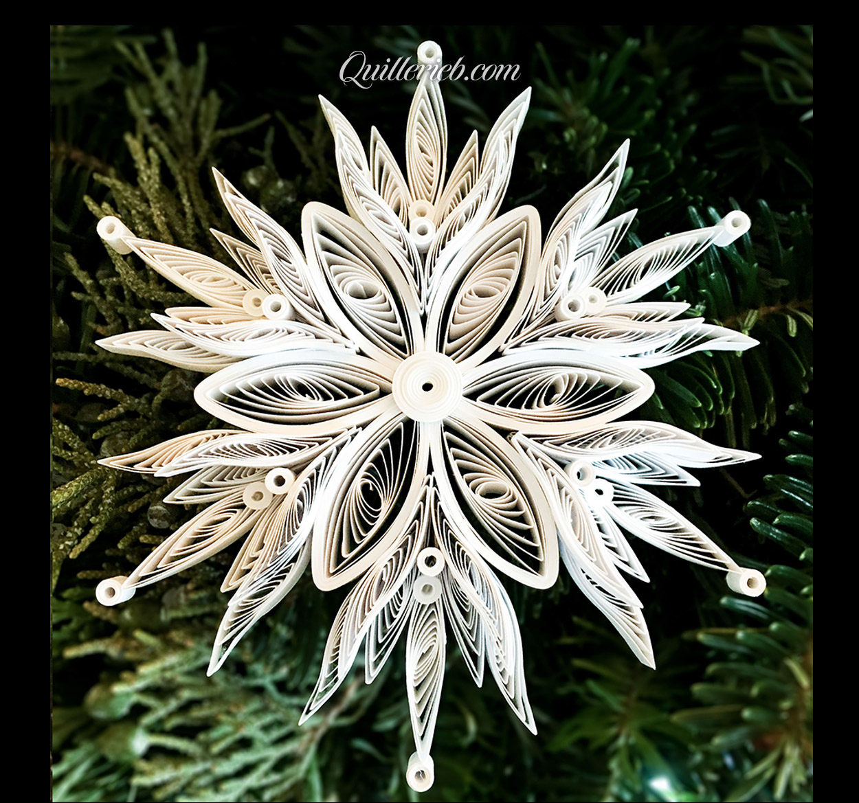  Quilling in white, 5th snowflake design full view against pine wreath backdrop.